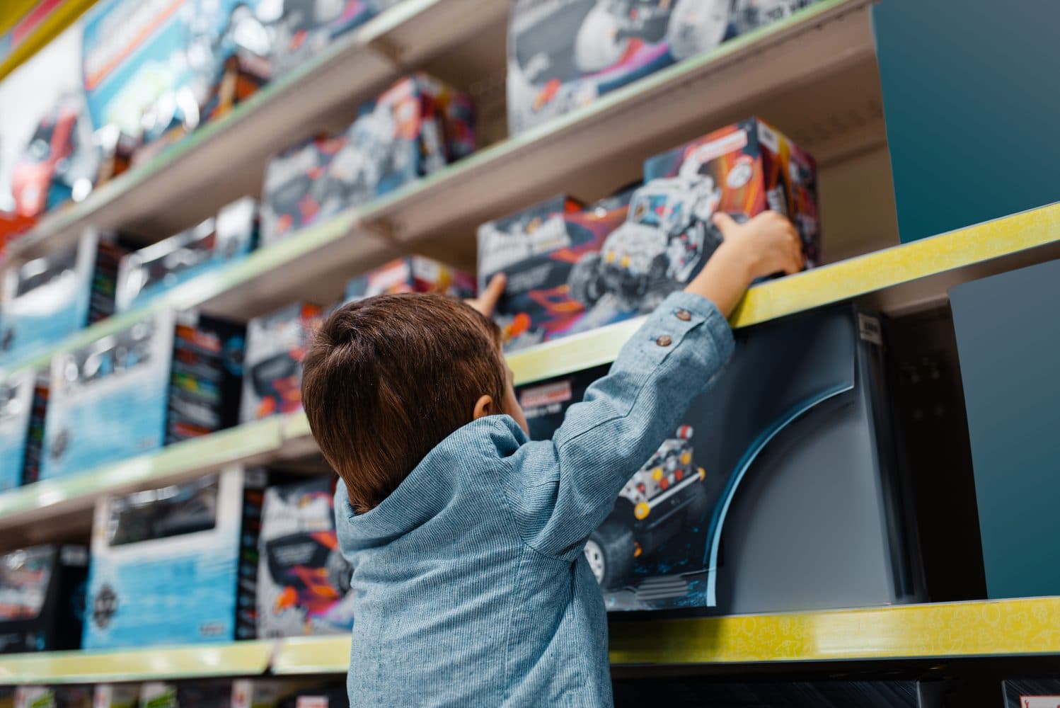 A child reaching for a boxed toy on a high shelf